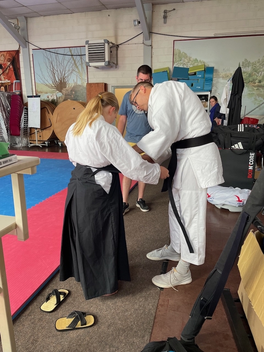 jeune aïkidoka aidée par le professeur pour enfiler son hakama